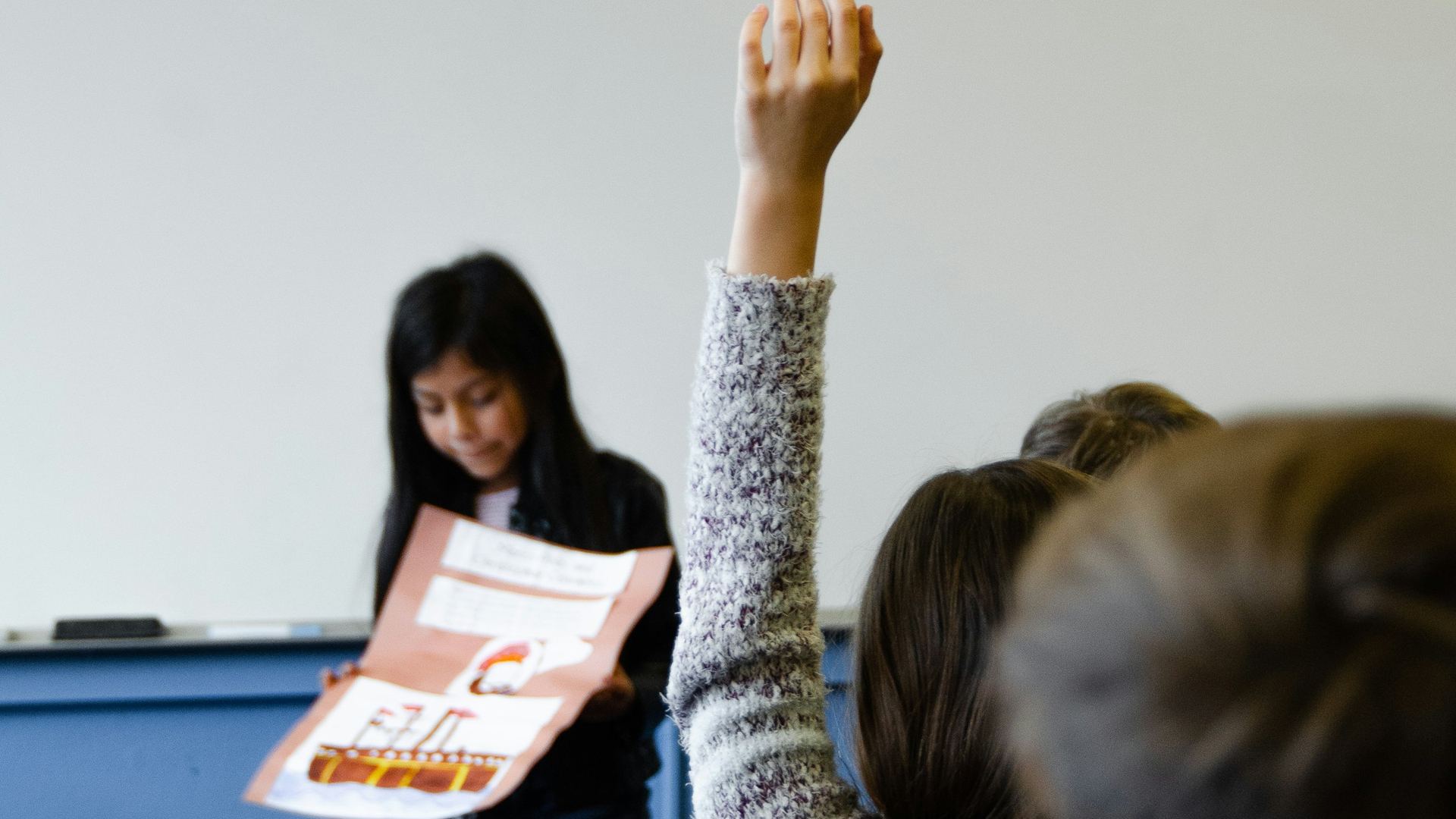 A student raises her hand in a classroom