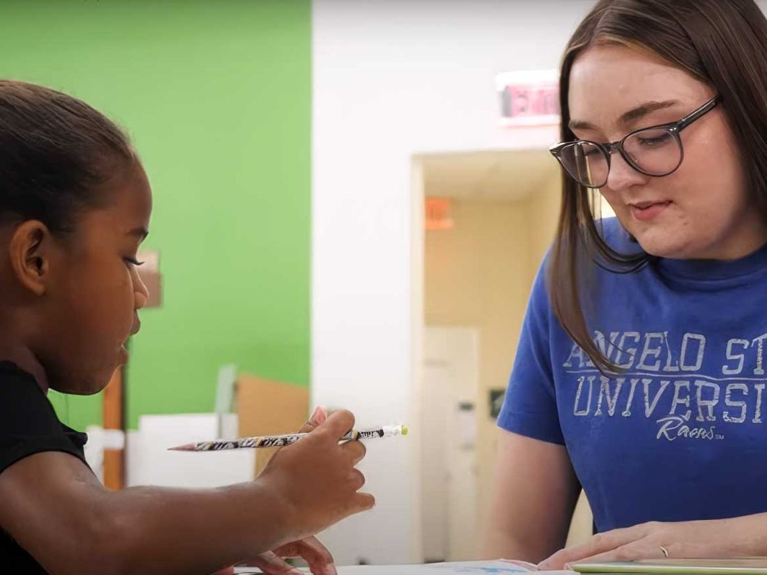 An Angelo State University student tutors a young girl at a table