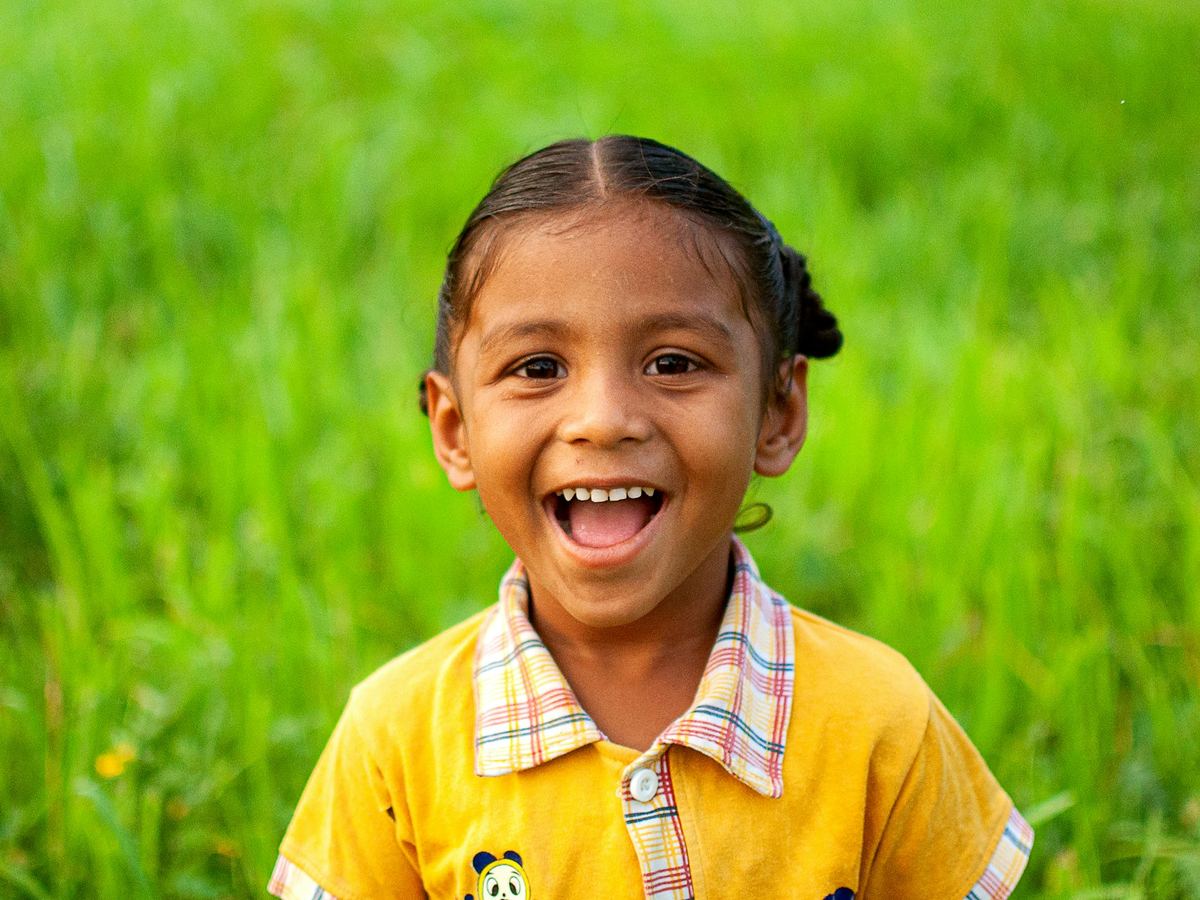 A laughing girl in a yellow shirt sits in green grass